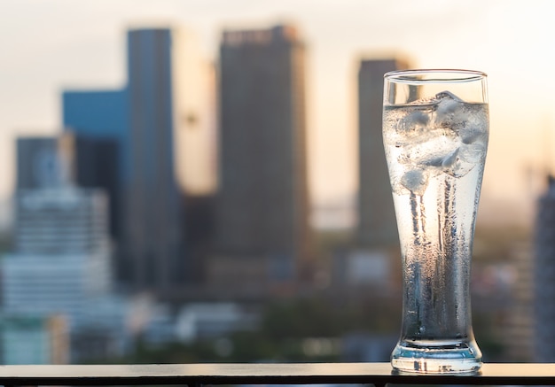 Copo transparente de água gelada no edifício da cidade desfocar o fundo