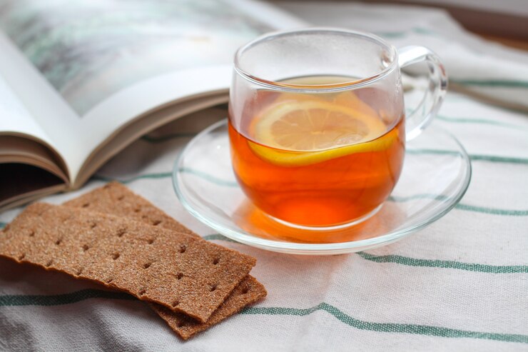 Copo transparente de chá com limão, pão torrado de centeio, um livro, luz natural, café da manhã