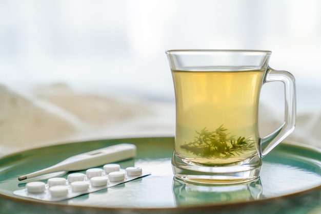 Copo transparente de vidro com chá de ervas e pastilhas de termômetro de folhas de grama, conceito de saúde