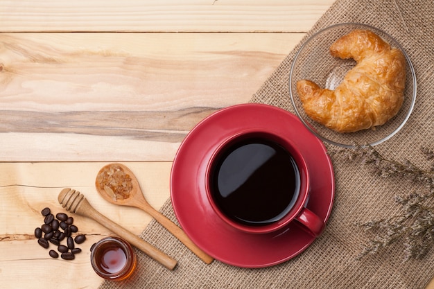 Copo vermelho café e açúcar na colher na serapilheira, grão de café na madeira mel e croissant flor seca