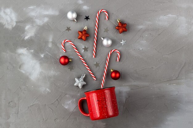 Copo vermelho com bastão de doces, bola e estrelas em fundo cinza. Conceito de celebração de Natal e ano novo.