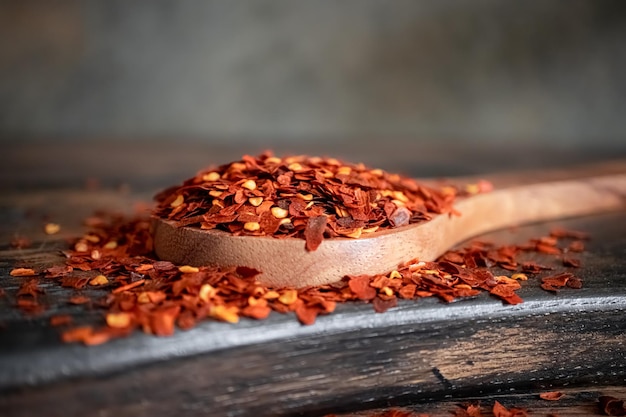 Copos de ají rojo picante en primer plano de una cuchara de madera sobre una mesa de cocina.