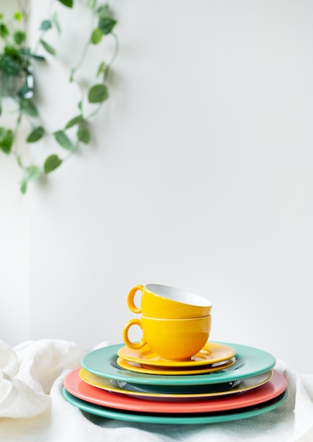 Copos amarelos vazios e pratos de cores brilhantes em uma mesa branca coberta com uma toalha de mesa de linho um vaso de flores na parede no fundo foto vertical