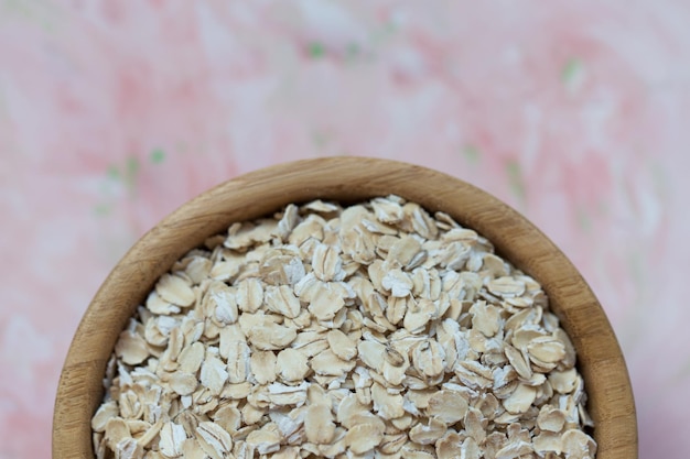 Copos de avena crudos en un cuenco de madera sobre un concepto de fondo rosa de alimentación saludable comida vegana cerca