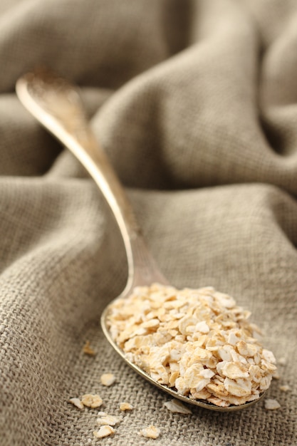 Copos de avena en cuchara de metal sobre fondo de tela de saco