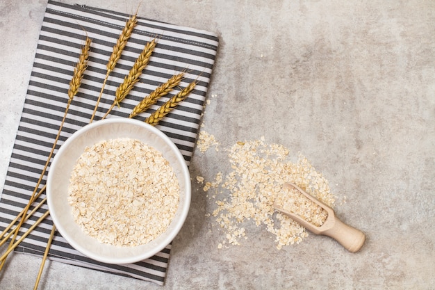 Copos de avena en un cuenco de cerámica blanca con una cuchara de madera sobre una mesa de mármol en una vista superior