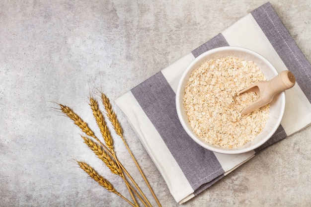 Copos de avena en un cuenco de cerámica blanca con una cuchara de madera en una vista superior