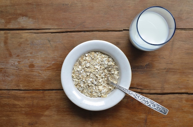 Copos de avena en recipiente blanco y leche en vidrio azul sobre la mesa de madera vintage