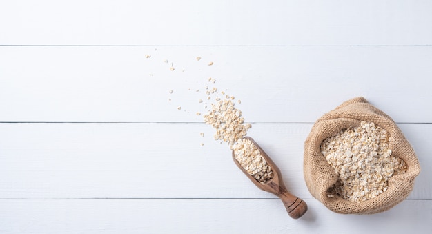 Copos de avena en saco con cuchara de madera sobre la mesa de madera blanca