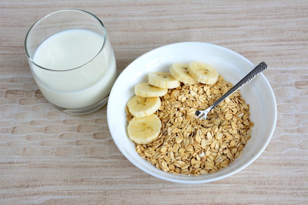 copos de avena en tazón blanco con rodajas de plátano y vaso de leche