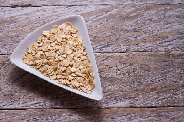 Copos de avena en un tazón blanco sobre una mesa de madera