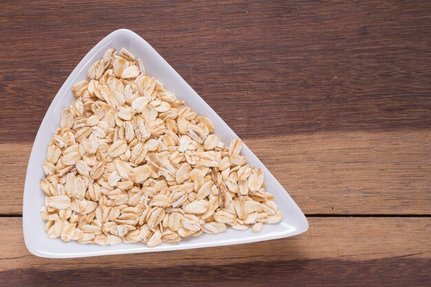 Copos de avena en un tazón blanco sobre una mesa de madera