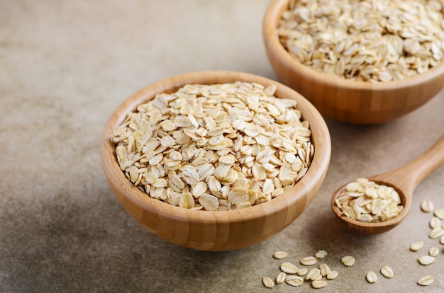 Copos de avena en un tazón de madera y cuchara de madera en marrón claro