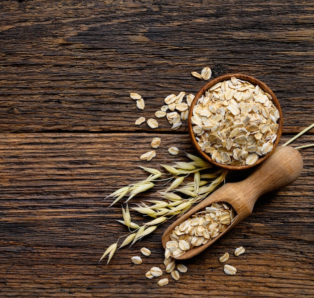 Copos de avena en un tazón de madera con cuchara y planta de avena sobre fondo de madera de tablón rústico antiguo. Espacio de copia de vista superior