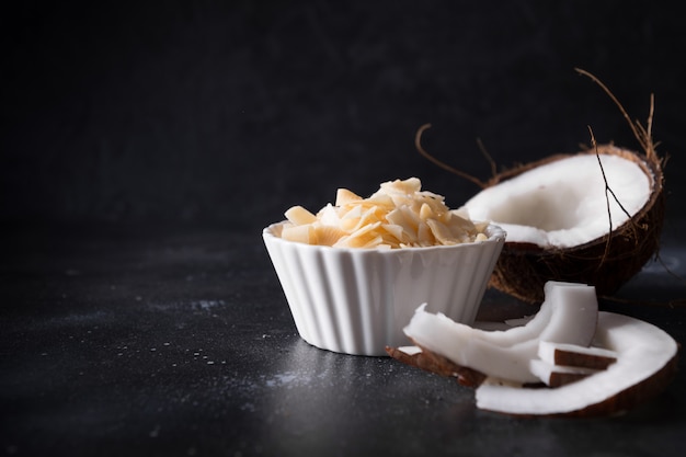 Copos de chips de coco orgánicos con azúcar y sal en un tazón blanco sobre negro Copia espacio