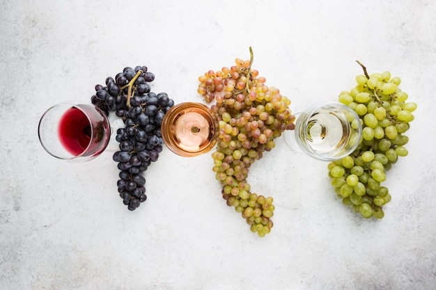 Copos com vinho branco, tinto e rosa e uvas maduras em fundo de pedra, vista superior