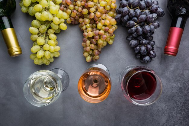 Copos com vinho branco, tinto e rosa e uvas maduras em fundo preto de pedra, vista superior