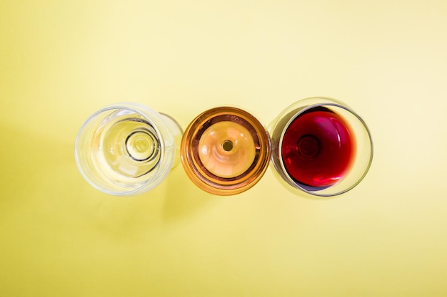 Copos com vinho branco vermelho e rosa na vista superior do fundo amarelo