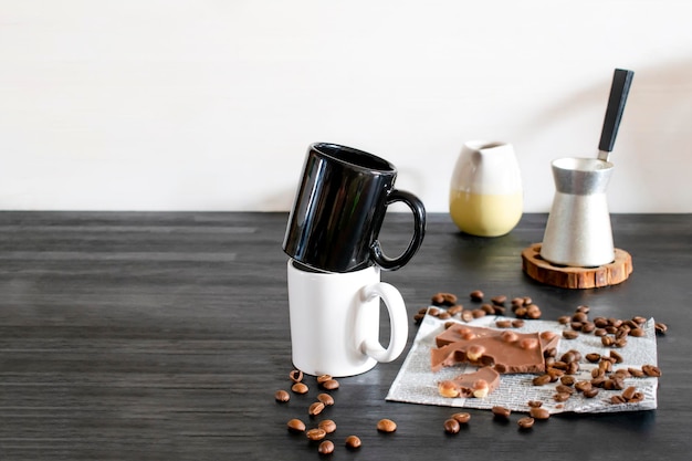 Copos de café expresso preto branco canecas grãos de café chocolate na mesa da cozinha utensílios louça cafeteira na prateleira de madeira preta manhã casa francesa bebida quente café da manhã espaço de cópia