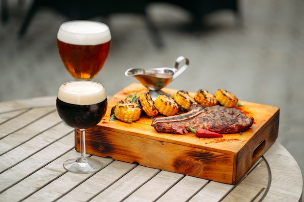 Foto copos de cerveja dourada e escura com bife grelhado em bandeja de madeira