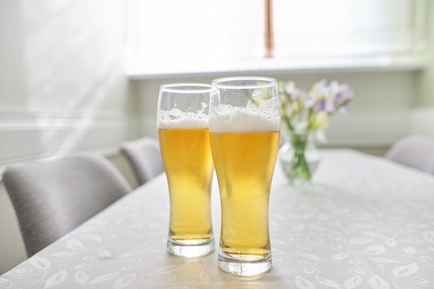 Copos de cerveja na mesa, mesa em casa com cadeiras perto da janela