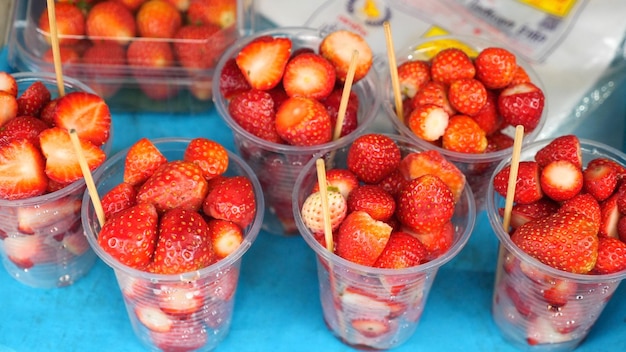 Copos de plástico com morangos vermelhos frescos no mercado de frutas Mercado de agricultores locais com frutas e bagas orgânicas Morangos recém-colhidos em copos porcionados para comer e ir