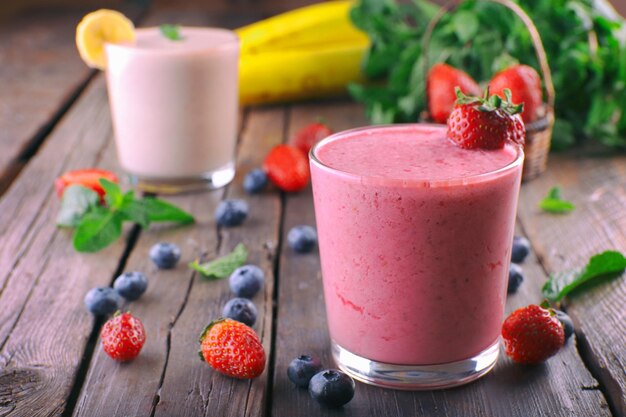 Copos de smoothie frio fresco com frutas e bagas em fundo de madeira