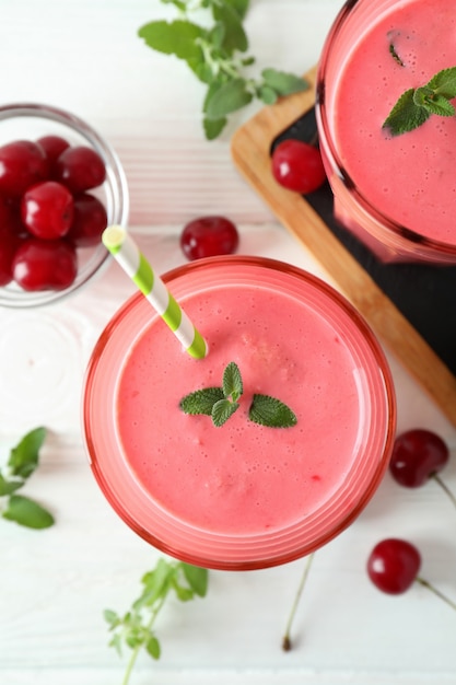 Copos de suco de cereja e ingredientes na mesa de madeira branca