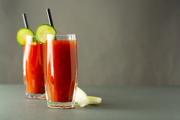 Copos de suco de tomate saboroso isolado na mesa cinza