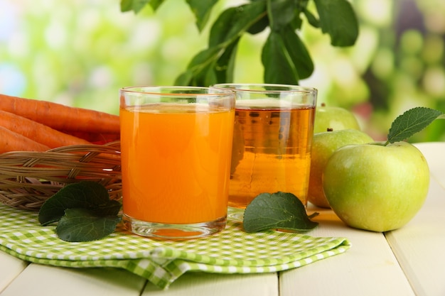 Copos de suco, maçãs e cenouras na mesa de madeira branca