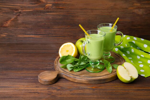 Copos de suco verde saudável com frutas e ervas na mesa de madeira