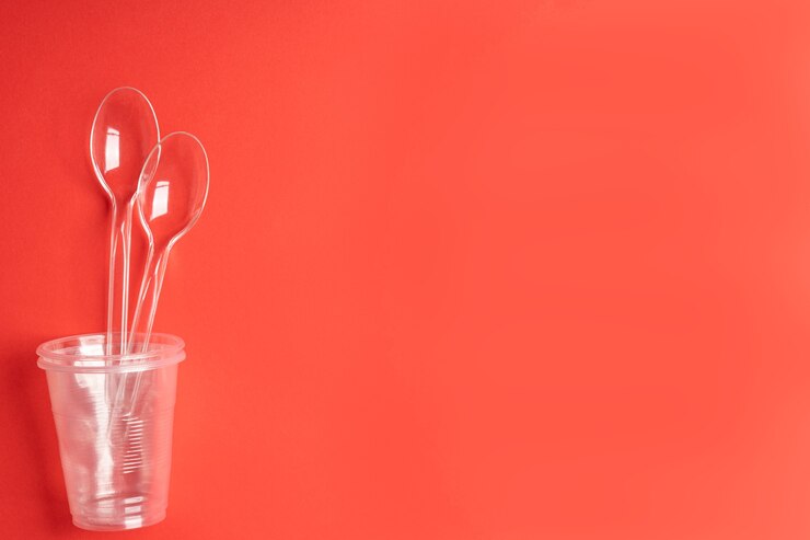 Copos e colheres descartáveis transparentes em um fundo vermelho. Regime de bebida. Coloque para texto