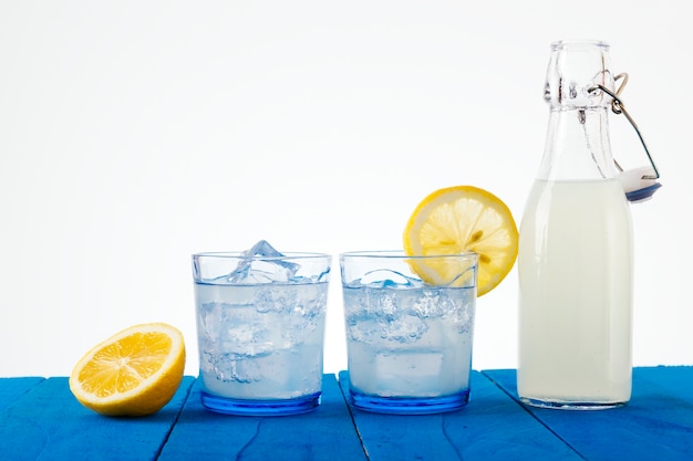 Copos e garrafa de limonada refrescante em uma mesa rústica azul