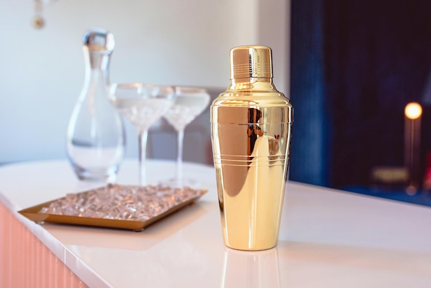 copos elegantes de decantador de vidro shaker dourado com coquetel e gelo no fundo bege
