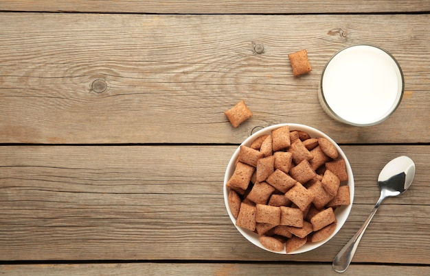 Copos de maíz de las almohadillas de chocolate en un tazón con leche sobre fondo azul. Textura de cereales.