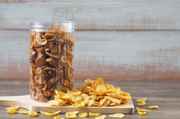 Copos de maíz de caramelo (grano entero) en paquete de tarro de plástico sobre mesa de madera.