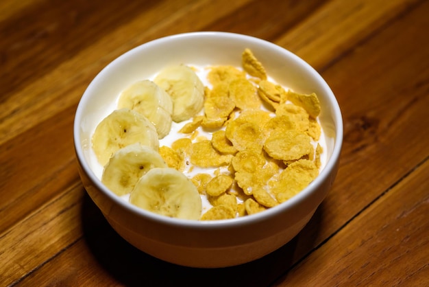 Copos de maíz cereales con leche y rodajas de plátano en un tazón sobre la mesa de madera