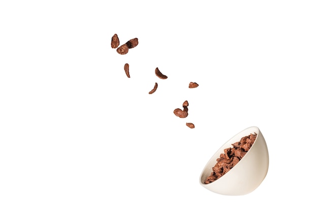 Copos de maíz de chocolate cayendo al cuenco blanco aislado en blanco. Movimiento. Copyspace.