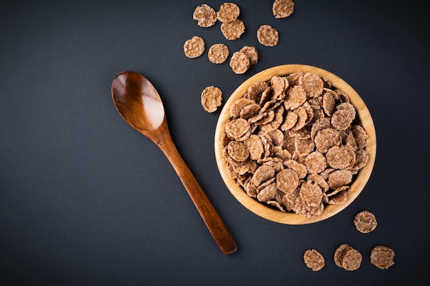 Copos de maíz de chocolate para el desayuno en un plato de bambú sobre una superficie oscura. Enfoque selectivo.