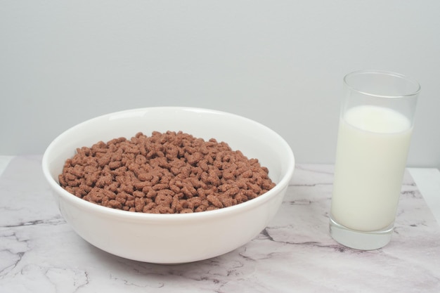 Copos de maíz de chocolate en un recipiente y un vaso de leche en la mesa