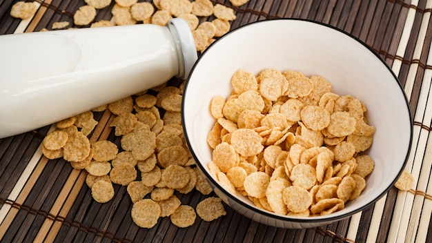 Copos de maíz saludables y leche en una servilleta de bambú. Botella de vidrio con leche para un desayuno saludable.