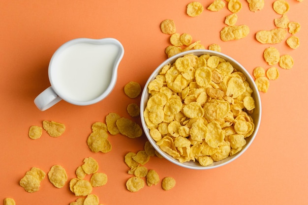 Copos de maíz en un tazón blanco y leche sobre fondo naranja