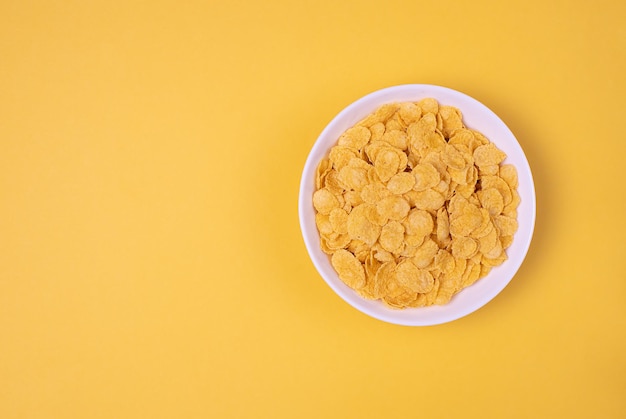 Copos de maíz en un tazón blanco sobre fondo amarillo para alimentos saludables de cereales. Vista superior. Copiar, espacio vacío para texto