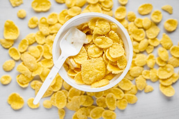 Copos de maíz con yogur en un tazón blanco con una cuchara sobre fondo blanco de madera