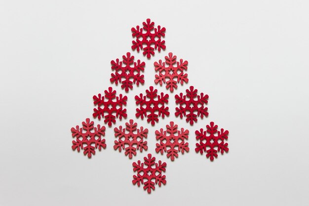 Copos de nieve hechos a mano de madera roja dispuestas como árbol de Navidad sobre superficie blanca