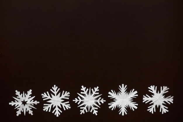 Copos de nieve de papel blanco de diferentes formas y tamaños sobre fondo de cartón marrón Vista superior