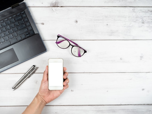 Copos para laptop, xícara de café e duas canetas, vista superior do espaço de trabalho do escritório e espaço para cópia do smartphone com a mão