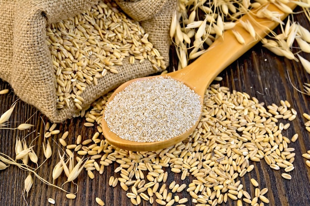 Copos de salvado de avena en cuchara, una bolsa de avena de grano, espigas de avena en el fondo de tablas de madera