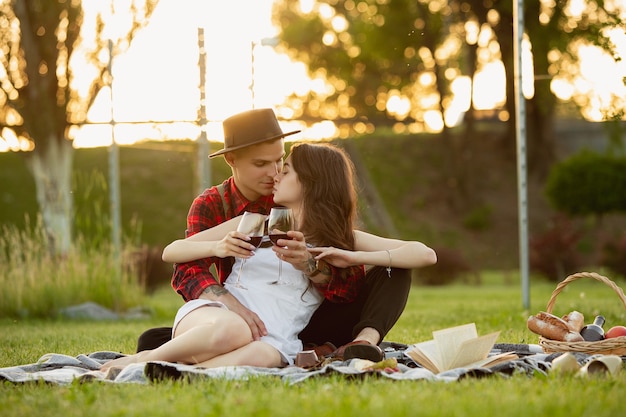 Copos tilintando. Casal jovem caucasiano aproveitando o fim de semana juntos no parque num dia de verão. Parece adorável, feliz, alegre. Conceito de amor, relacionamento, bem-estar, estilo de vida. Emoções sinceras.