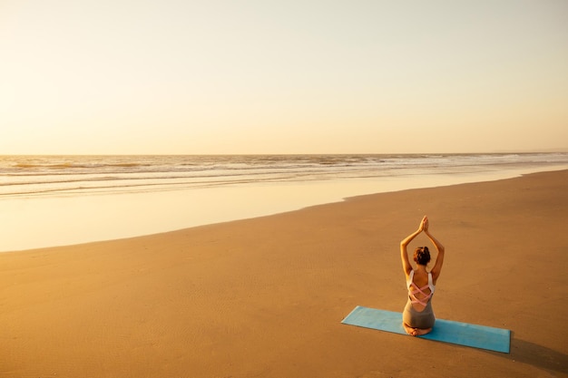 Copyspace mujer haciendo yoga realizando asanas y disfrutando de la vida al atardecer en el espacio de copia de mar de playa